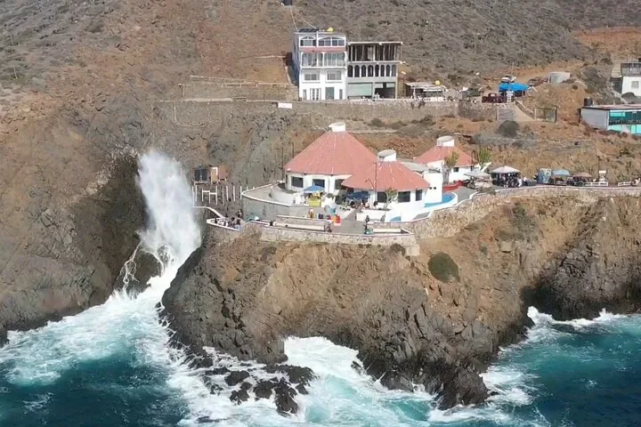 Wasser spritzt kraftvoll aus den Felsen nahe der Küstengebäude in La Bufadora.